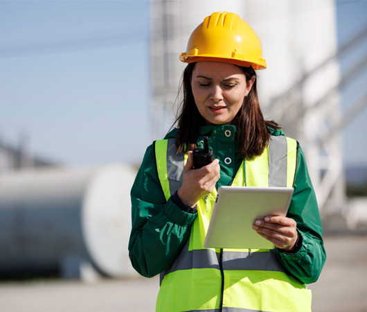 Portrait of a female engineer using walkie-talkie and digital tablet at industrial facility